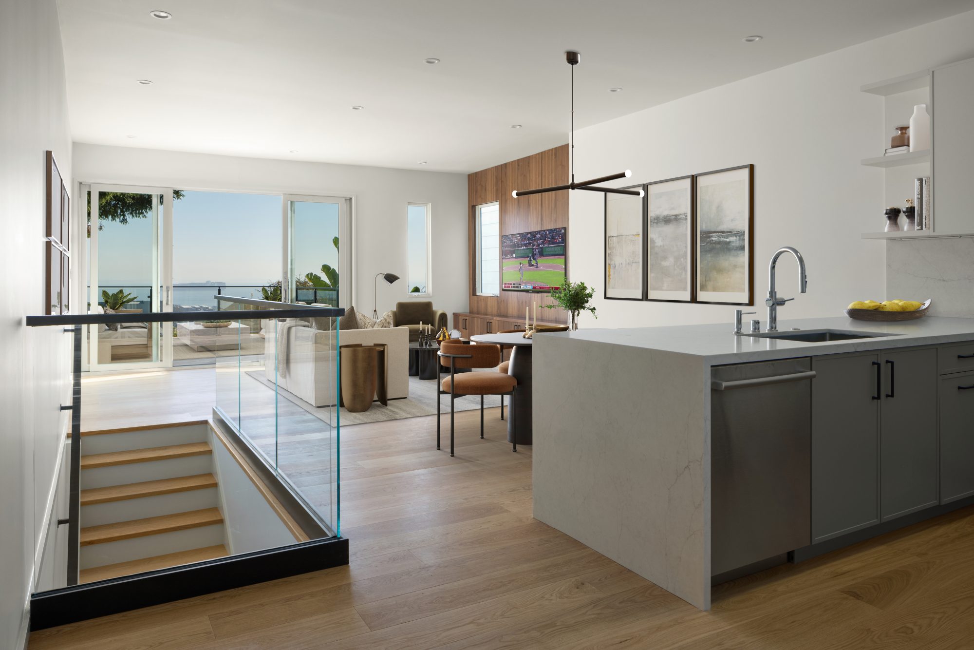 Open-plan kitchen, dining, and living with glass stair railing and bay views